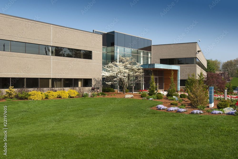 Immeuble de bureaux moderne avec pelouse, arbres et ciel bleu.