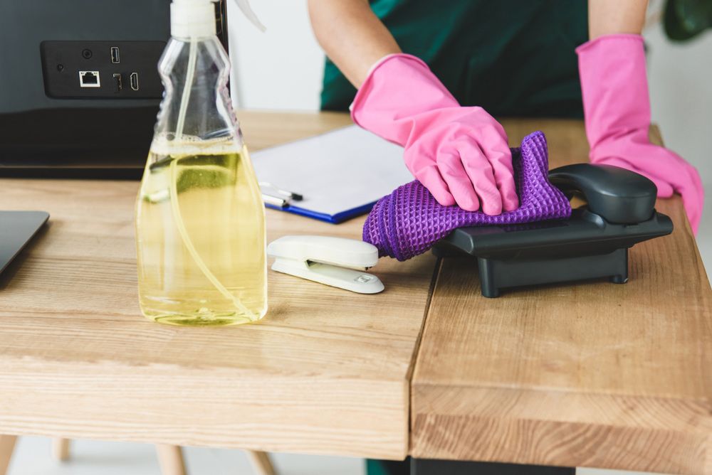 A Person Wearing Pink Gloves is Cleaning a Telephone on a Desk — Cleaning for Good in Tallebudgera, QLD