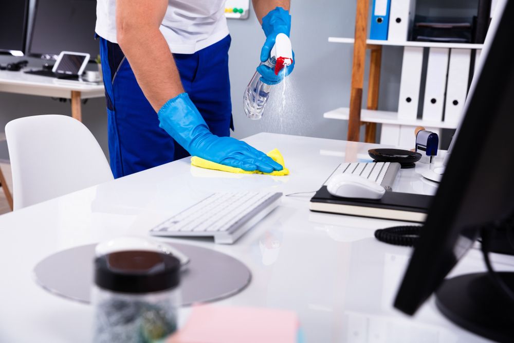 A Man is Cleaning a Desk in an Office With a Spray Bottle — Cleaning for Good in Tallebudgera, QLD