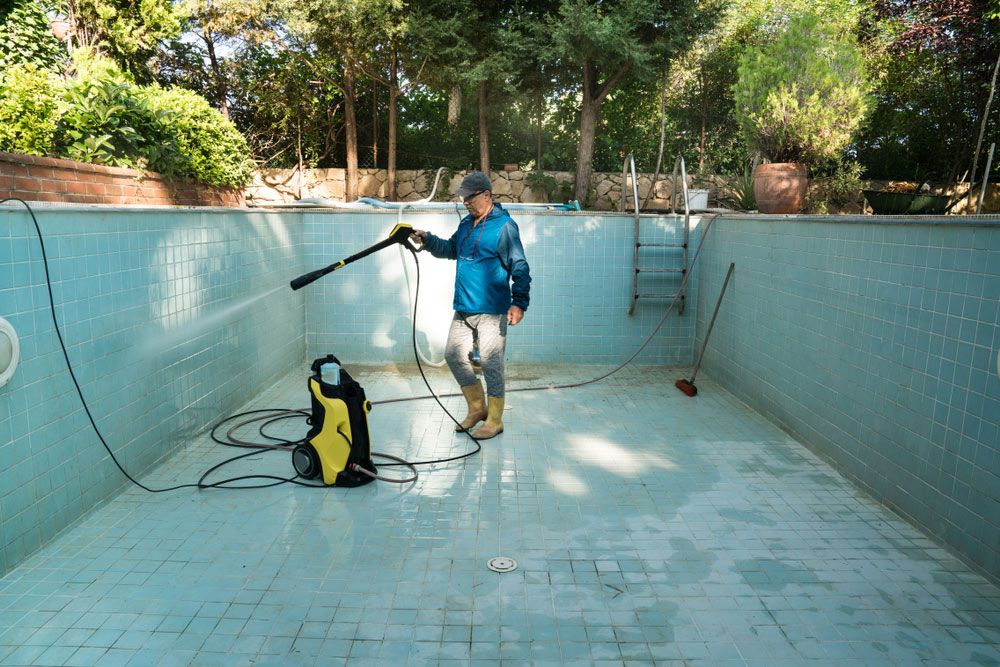 A Man is Cleaning an Empty Swimming Pool With a High Pressure Washer — Cleaning for Good in Tallebudgera, QLD