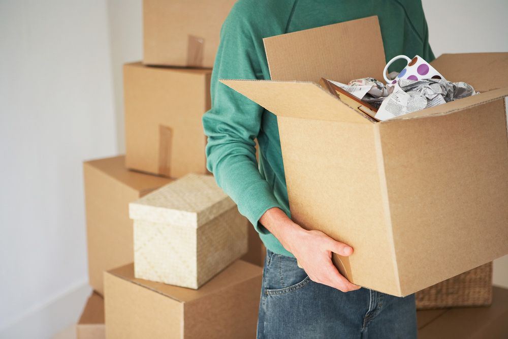 A Man in a Green Shirt is Holding a Cardboard Box Full of Clothes — Cleaning for Good in Palm Beach, QLD