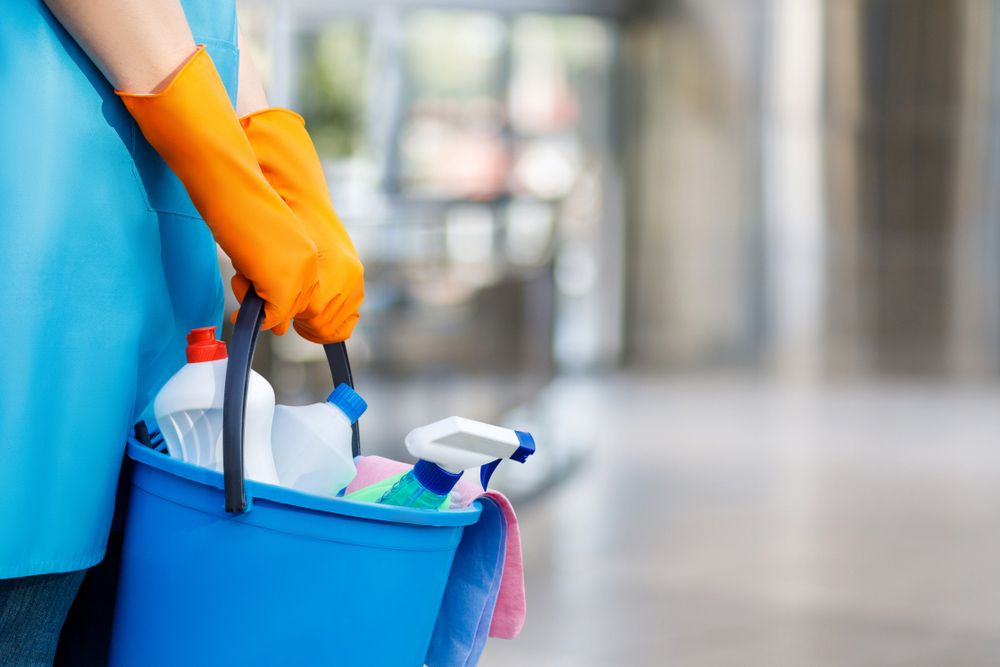 A Person Wearing Orange Gloves is Holding a Blue Bucket Filled With Cleaning Supplies — Cleaning for Good in Mullumbimby, NSW