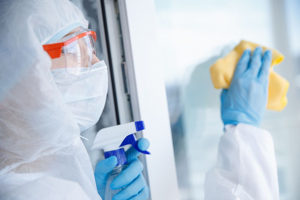A Person in a Protective Suit is Cleaning a Window With a Spray Bottle and a Cloth — Cleaning for Good in Tallebudgera, QLD