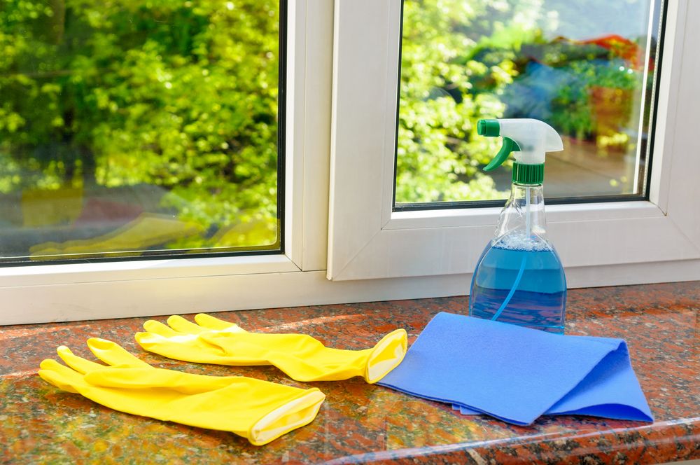 Yellow rubber gloves, blue cloth, and spray bottle on windowsill with greenery visible — Cleaning for Good in Currumbin, QLD