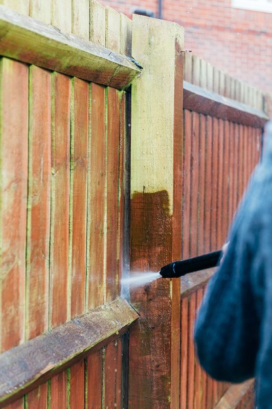 A Person is Cleaning a Wooden Fence With a High Pressure Washer — Cleaning for Good in Currumbin, QLD
