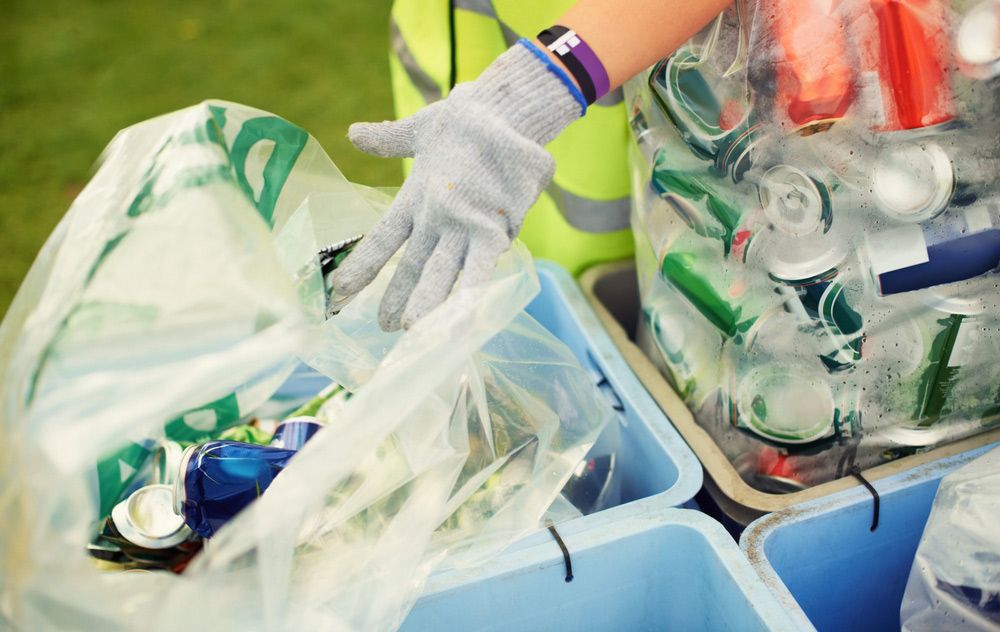A Person Wearing Gloves is Putting a Can Into a Recycling Bin — Cleaning for Good in Tallebudgera, QLD