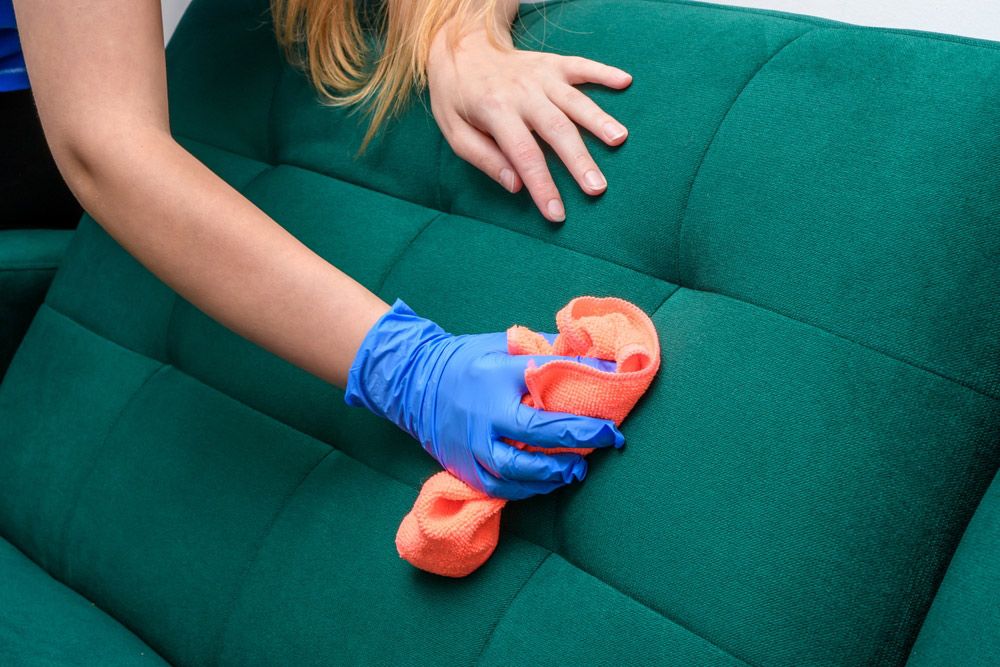 A Woman is Cleaning a Green Couch With a Cloth and Gloves — Cleaning for Good in Ballina, NSW