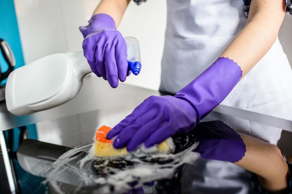 A Woman Wearing Purple Gloves is Cleaning a Stove With a Sponge and Spray — Cleaning for Good in Lennox Head, NSW
