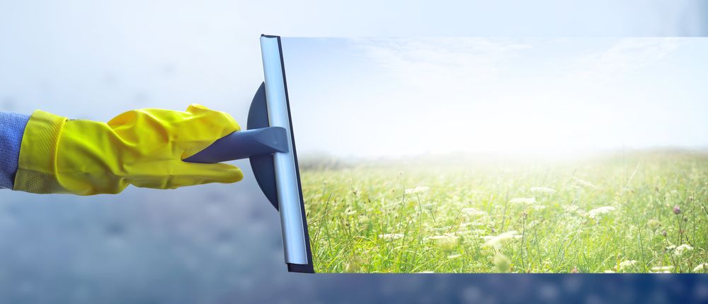 A Person Wearing Yellow Gloves is Cleaning a Window With a Squeegee — Cleaning for Good in Lennox Head, NSW