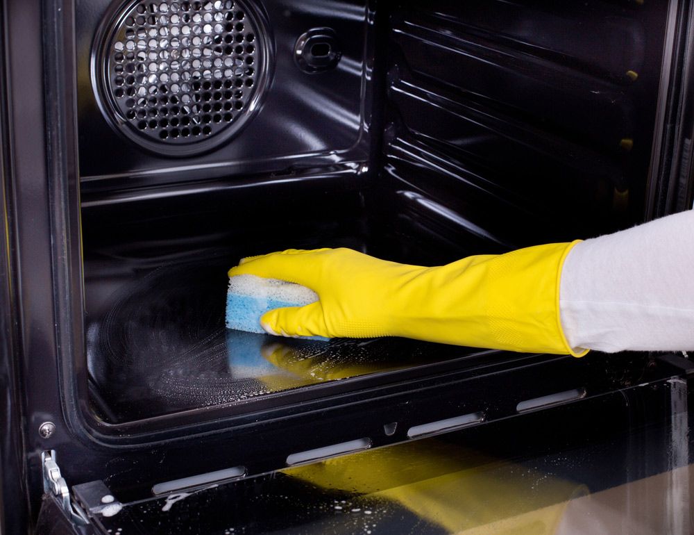 A Person Wearing Yellow Gloves is Cleaning an Oven With a Sponge — Cleaning for Good in Brunswick Heads, NSW