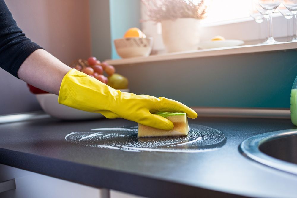 A Person Wearing Yellow Gloves is Cleaning a Kitchen Counter With a Sponge — Cleaning for Good in Port Macquarie, NSW