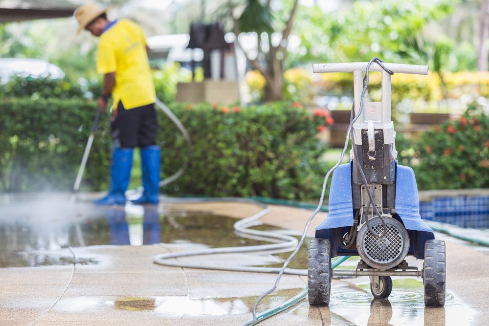 A Man is Using a High Pressure Washer to Clean a Concrete Floor — Cleaning for Good in Palm Beach, QLD