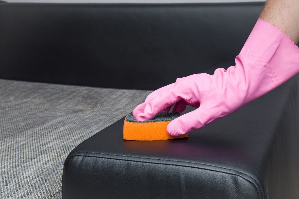 A Person Wearing Pink Gloves is Cleaning a Black Leather Couch With a Sponge — Cleaning for Good in Brunswick Heads, NSW