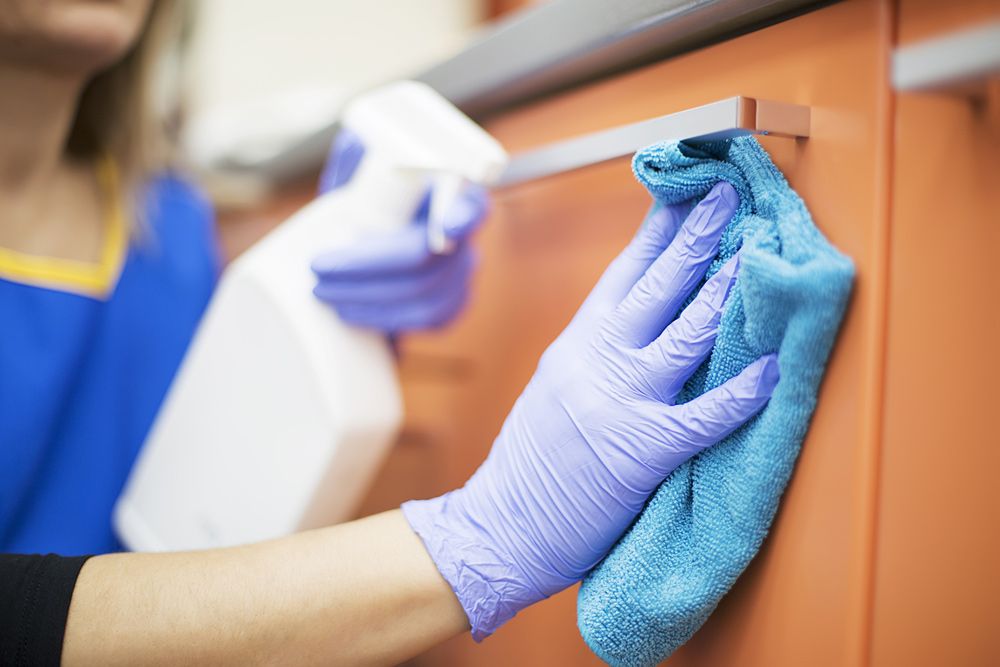 A Woman Wearing Purple Gloves is Cleaning a Cabinet With a Towel — Cleaning for Good in Brunswick Heads, NSW
