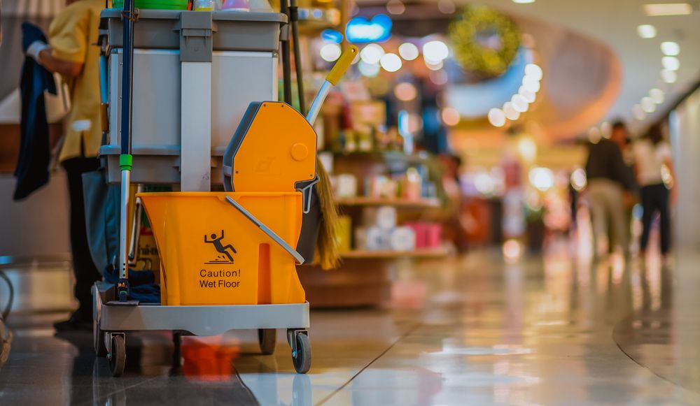A Cleaning Cart With a Yellow Bucket and Mop in a Mall — Cleaning for Good in Elanora, QLD