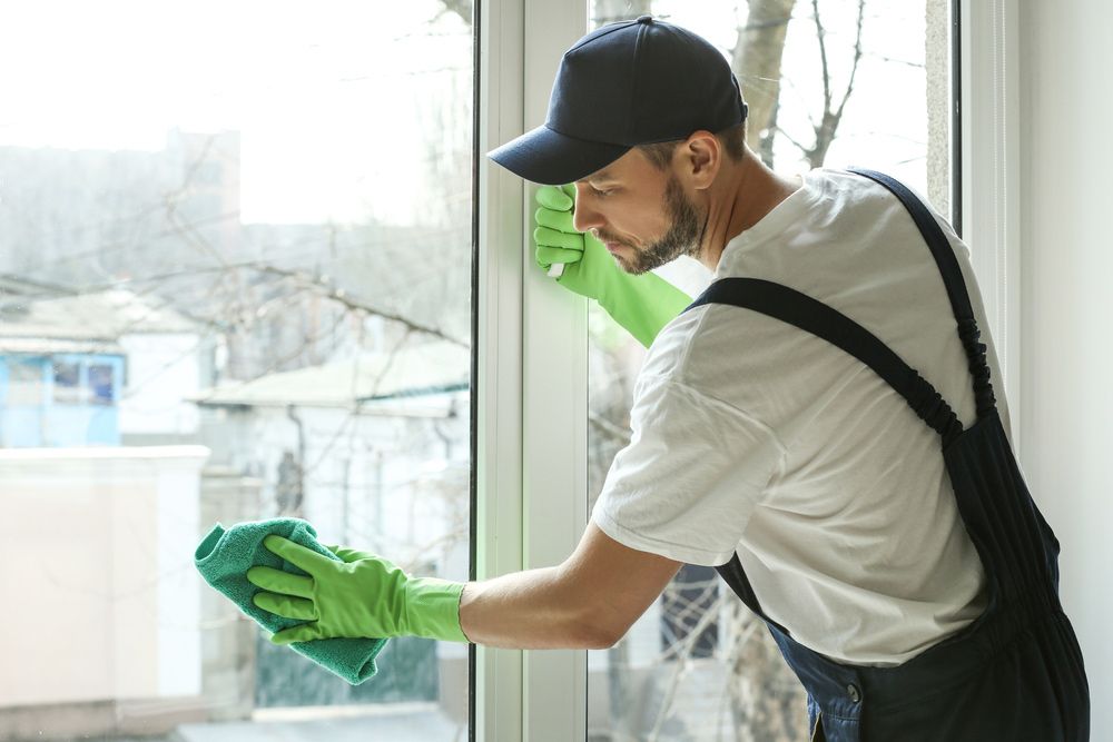A Man in Green Gloves is Cleaning a Window With a Cloth — Cleaning for Good in Palm Beach, QLD