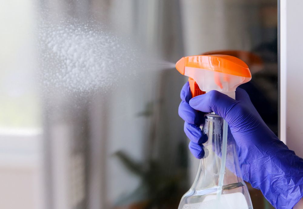 A Person Wearing Purple Gloves is Spraying a Spray Bottle on a Window — Cleaning for Good in Elanora, QLD