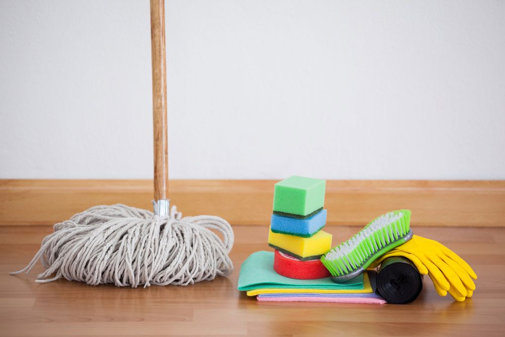 A Mop Sponges Brushes and Gloves Are on a Wooden Floor — Cleaning for Good in Byron Bay, NSW