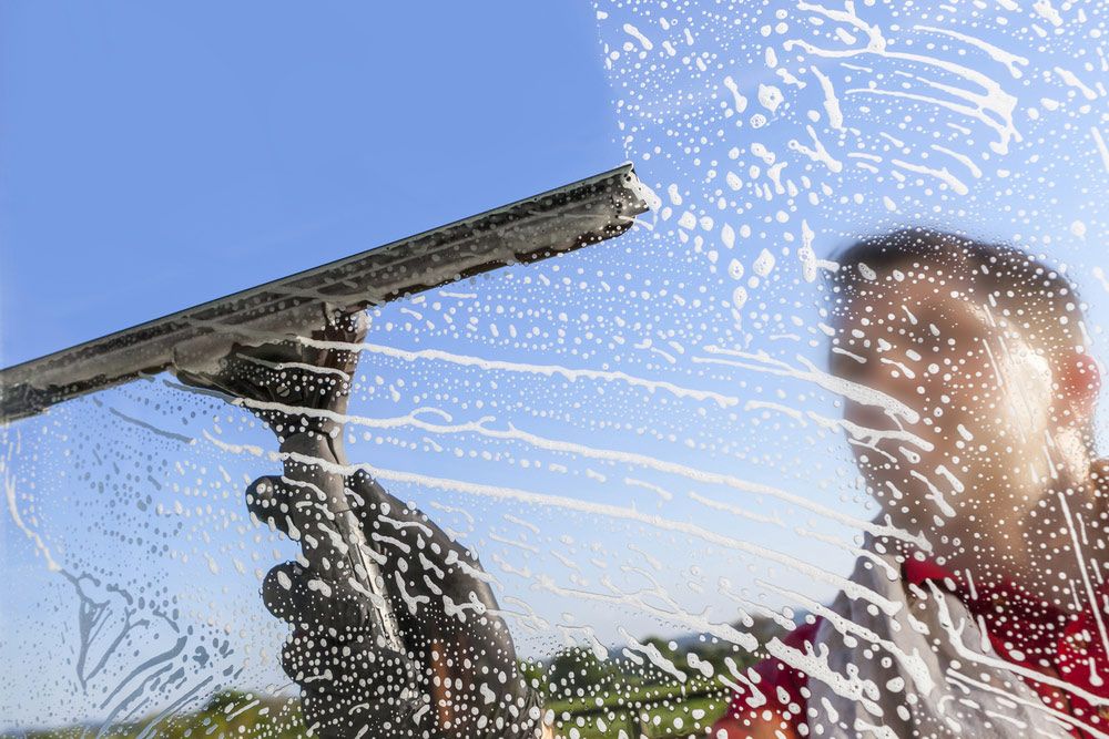 A Man is Cleaning a Window With a Squeegee — Cleaning for Good in Bangalow, NSW