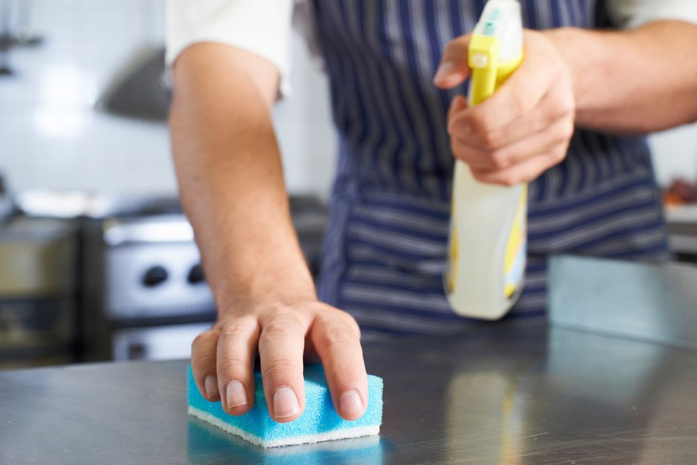 A Person is Cleaning a Counter With a Sponge and Spray Bottle — Cleaning for Good in Mullumbimby, NSW