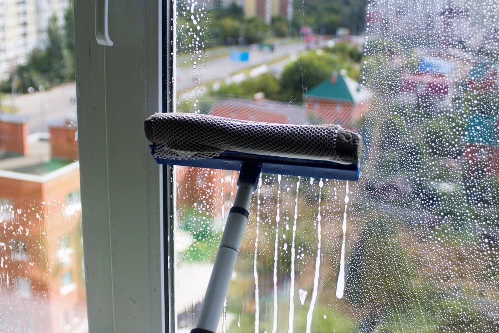 A Person is Cleaning a Window With a Squeegee — Cleaning for Good in Ocean Shores, NSW