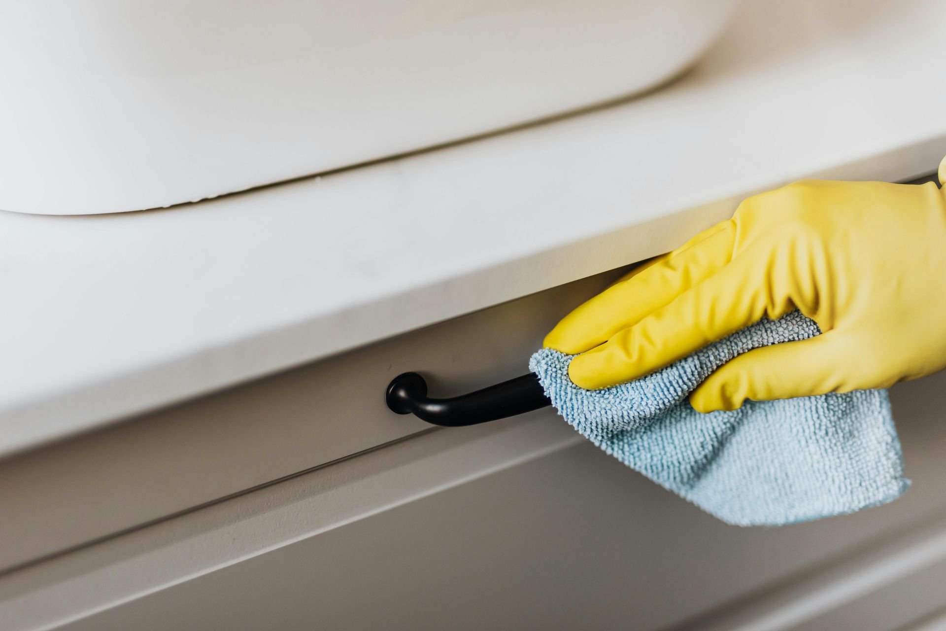 A Yellow Glove is cleaning a black handle of a drawer— Cleaning for Good in Byron Bay, NSW