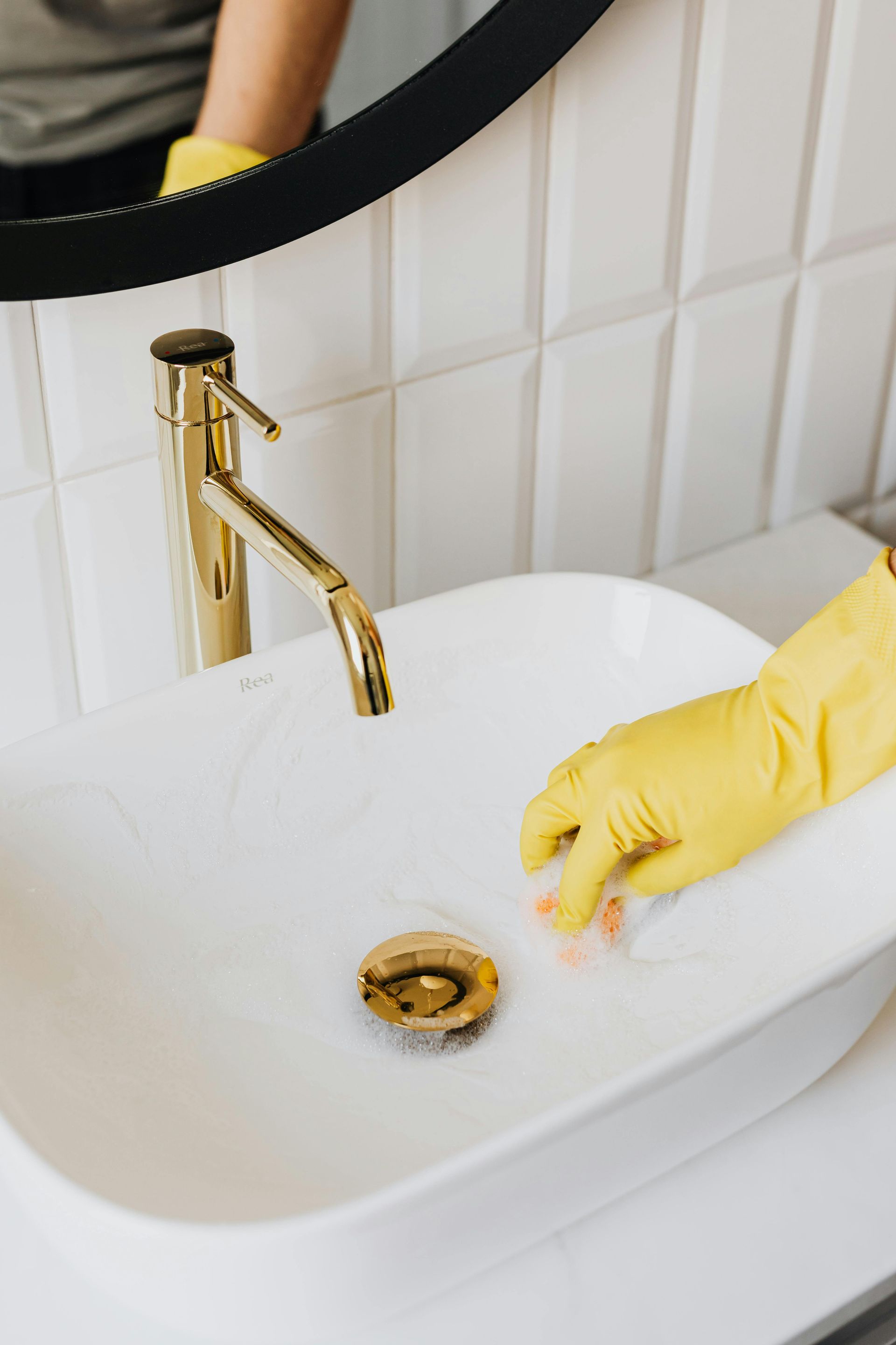 A Woman in Yellow Gloves is Cleaning a Gold Tap With a Cloth — Cleaning for Good in Byron Bay, NSW
