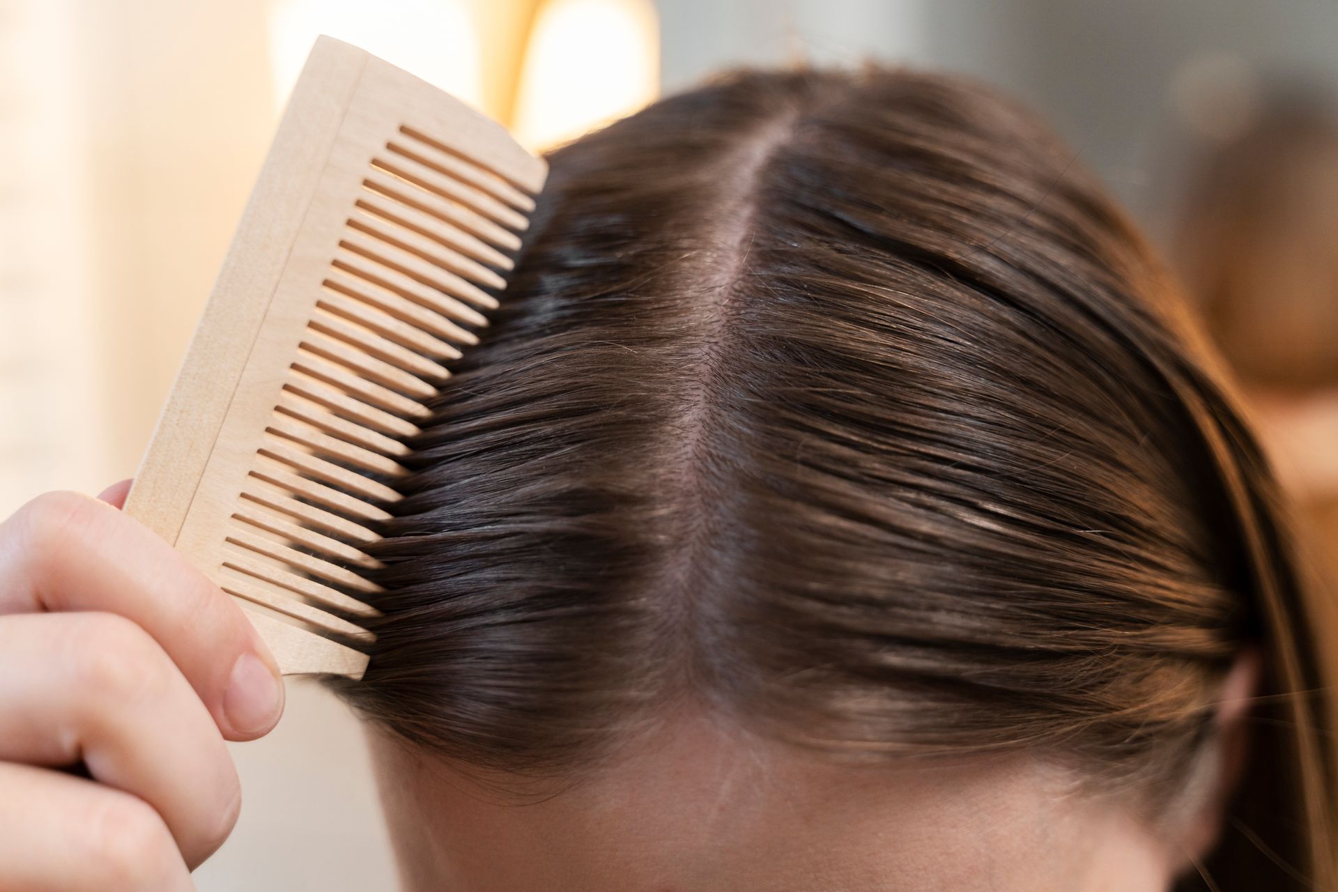 Hand combing a dark-haired scalp with visible parting, checking hair roots