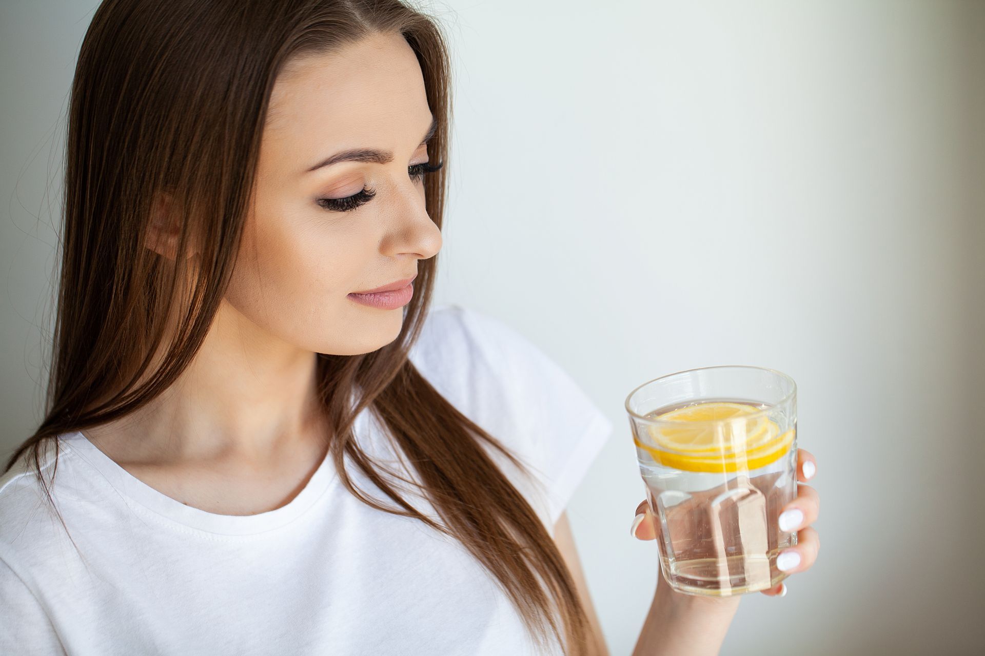 Woman holding a glass of water with lemon, looking at it indoors