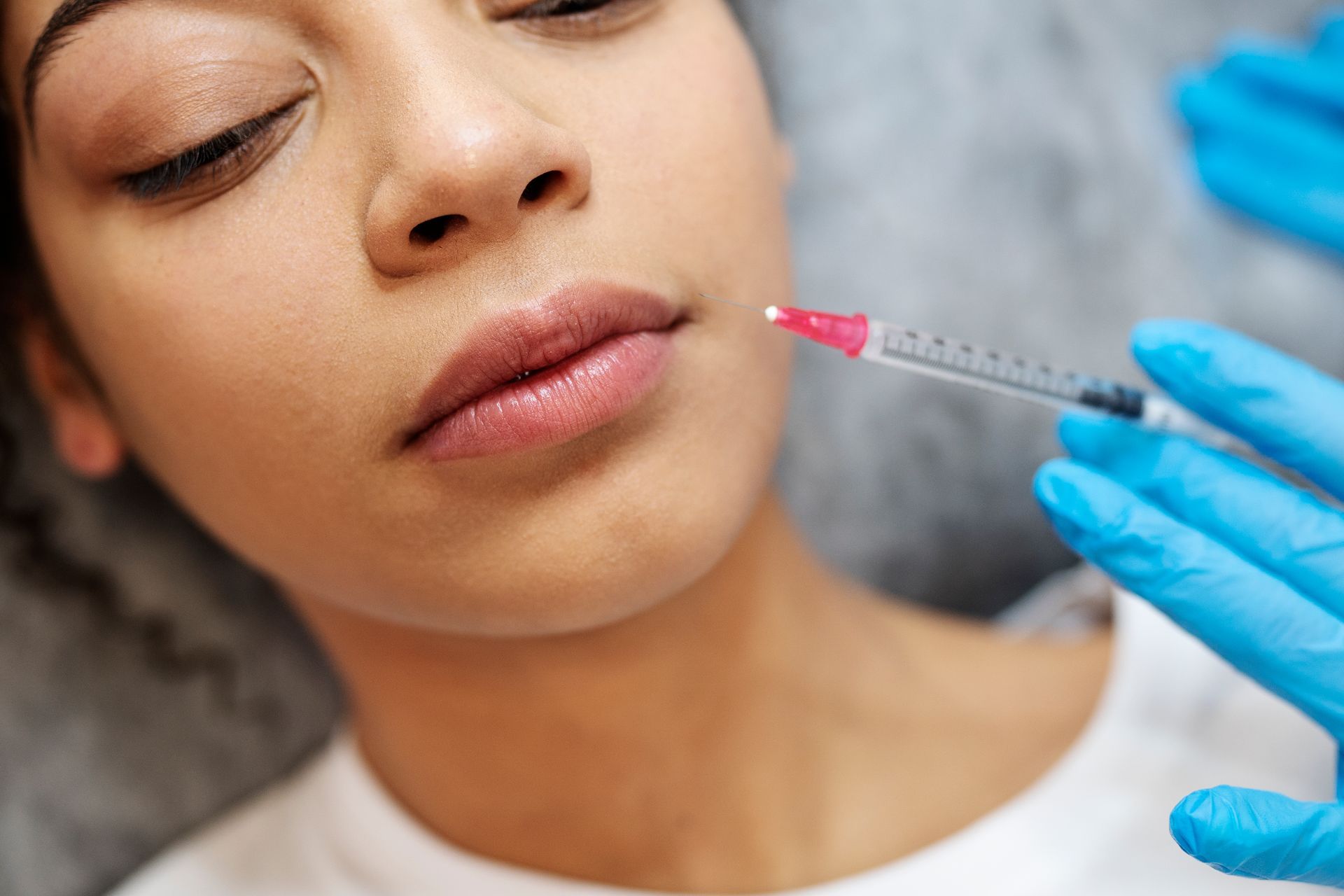 Cosmetic injection near a woman’s lips with a gloved hand holding a syringe
