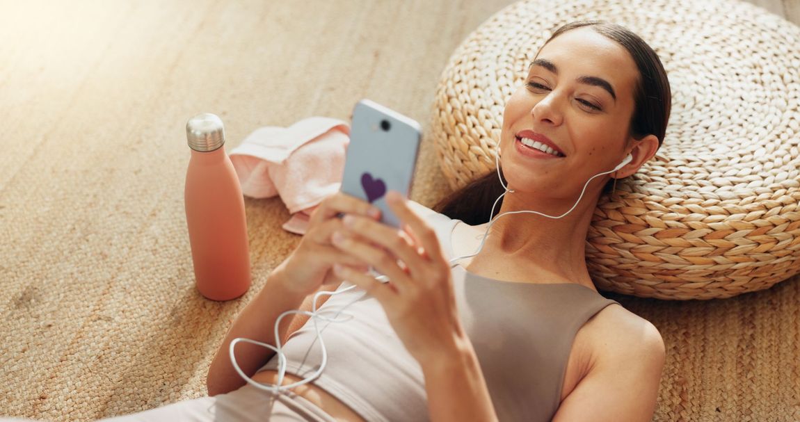 A woman is sitting on the floor listening to music on her phone.