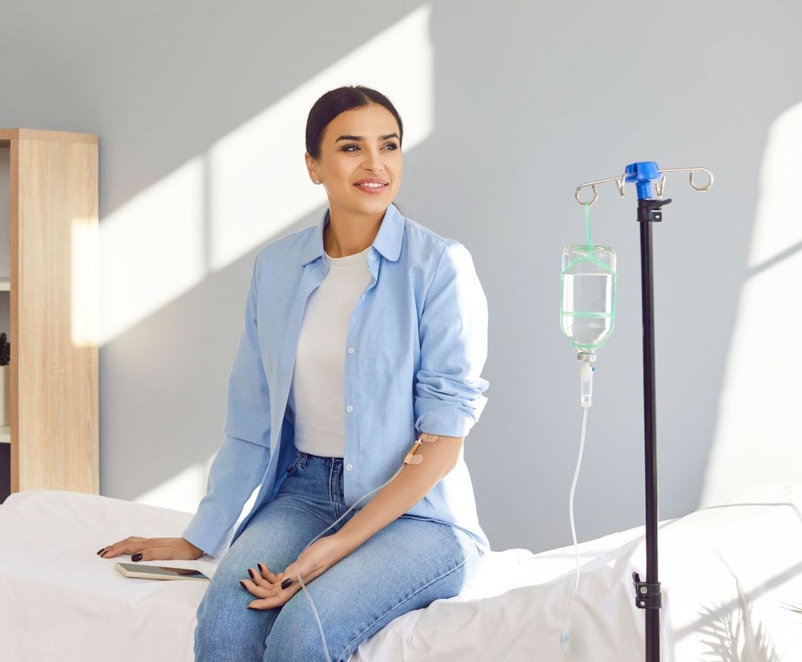 A woman is sitting on a bed with an iv in her arm.
