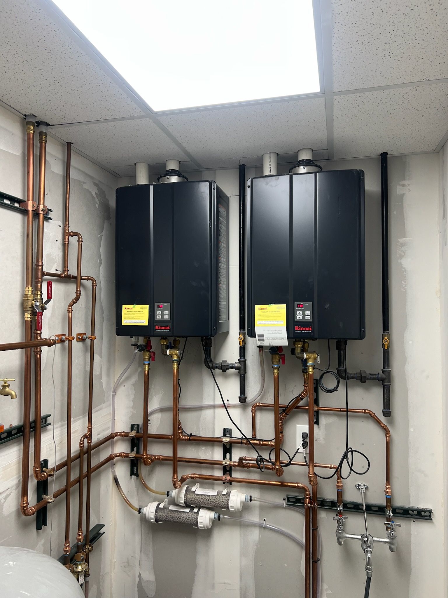 Two black wall-mounted boilers with copper pipes in a utility room