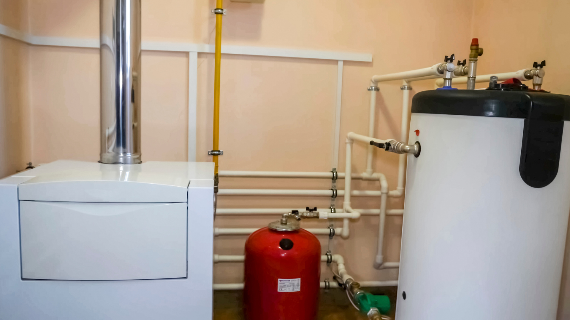 White wall-mounted tankless water heater with digital display above two pipes near a window