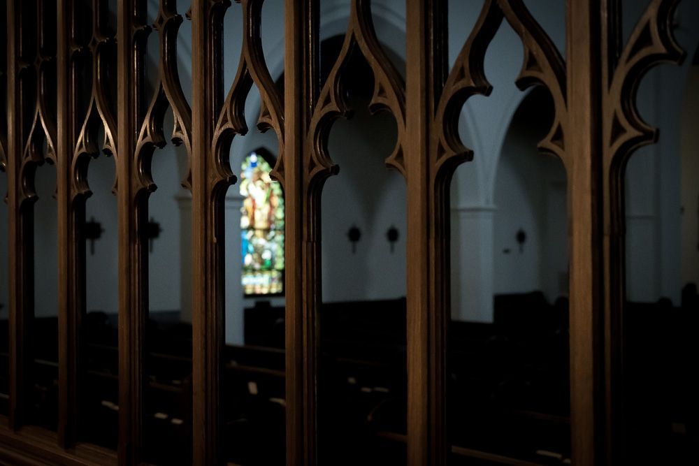 A stained glass window is behind a wooden fence in a church.
