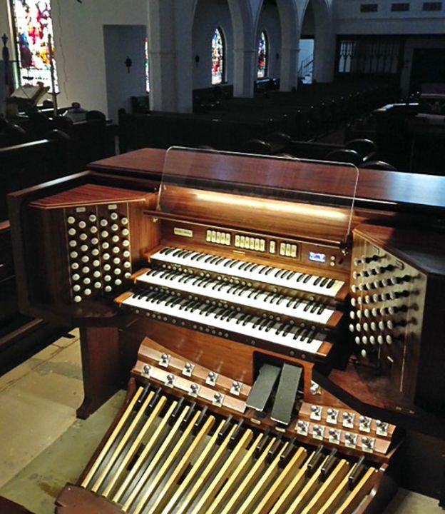 An organ in a church with a stained glass window in the background