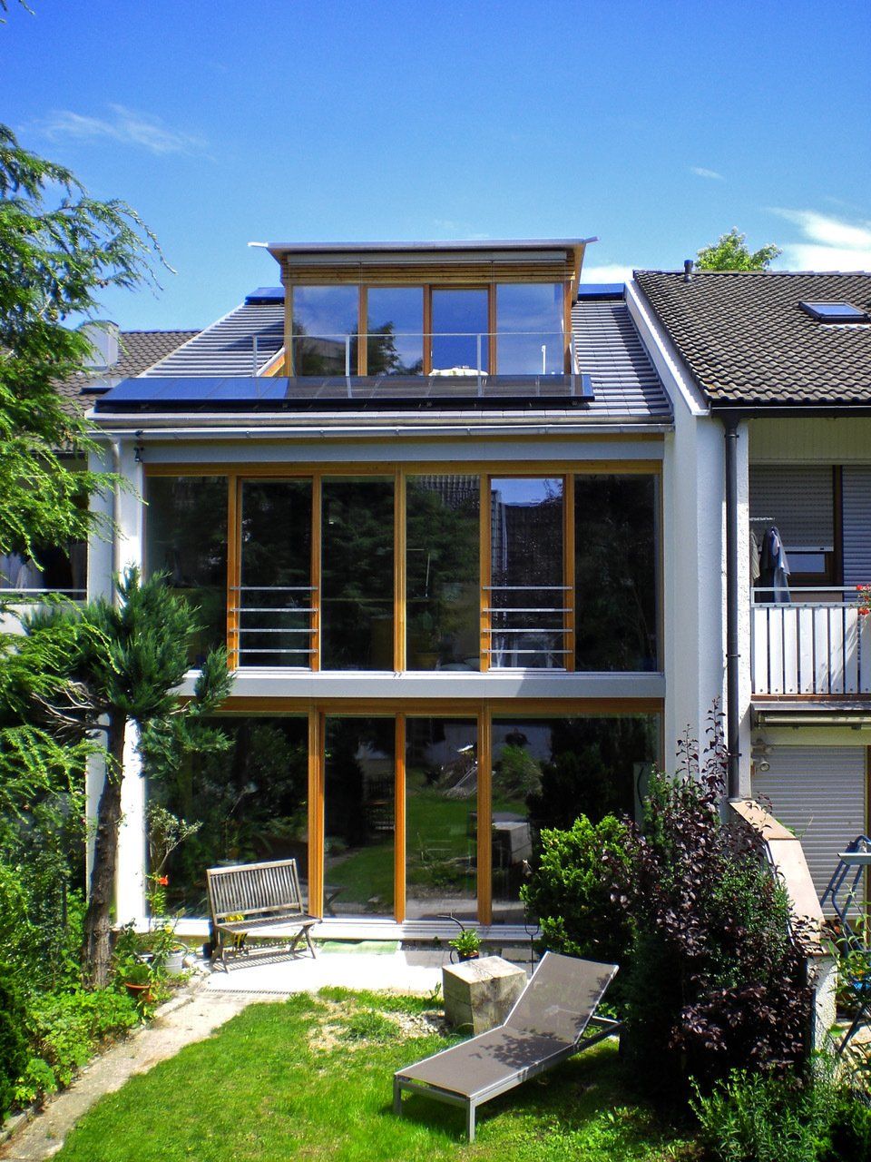 Modernes Haus mit großen Fenstern und Garten. Ausgestattet mit Solarpaneelen auf dem Dach.