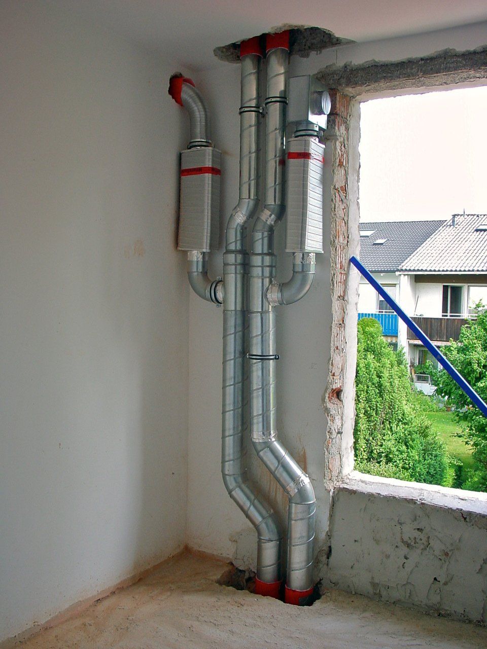 Verzinkte Metallrohre wurden in der Nähe eines Fensters installiert, das aus dem Gebäude führt. Rote Akzente.