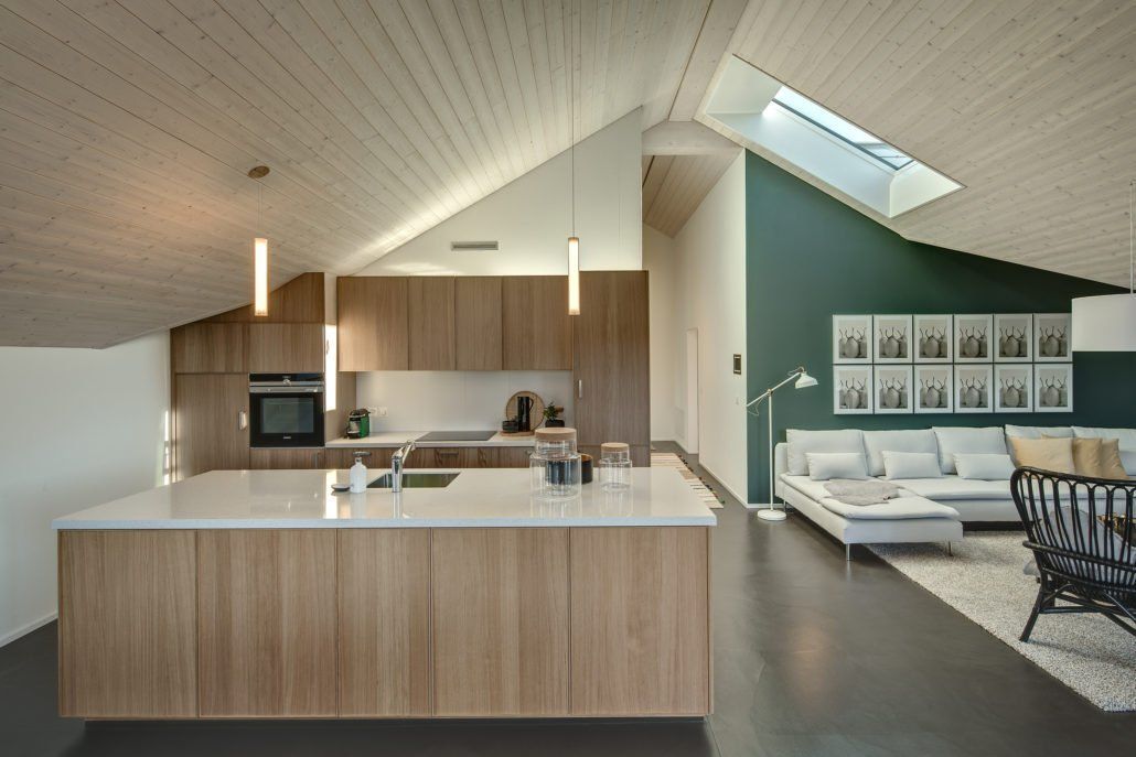 Moderne Küche mit Holzschränken, Kochinsel und hoher, schräger Decke mit Oberlicht.