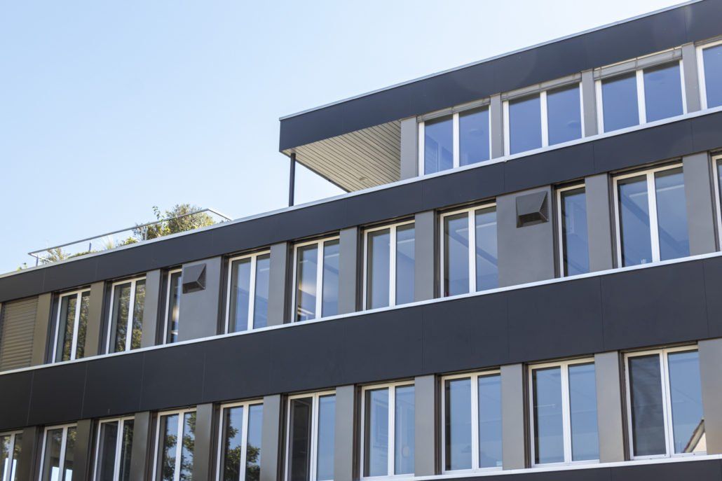 Modernes mehrstöckiges Gebäude mit dunkler Fassade, vielen Fenstern und Flachdach.