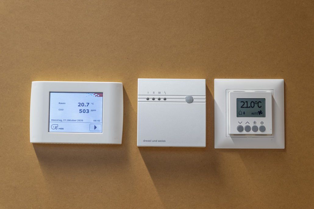 Drei weiße Thermostate, jeweils mit Digitalanzeige, sind an einer hellbraunen Wand angebracht.