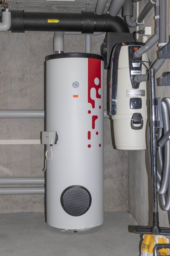 Weißer Warmwasserbereiter mit rotem Design neben einer Zentralstaubsaugeranlage in einem Industrieumfeld.