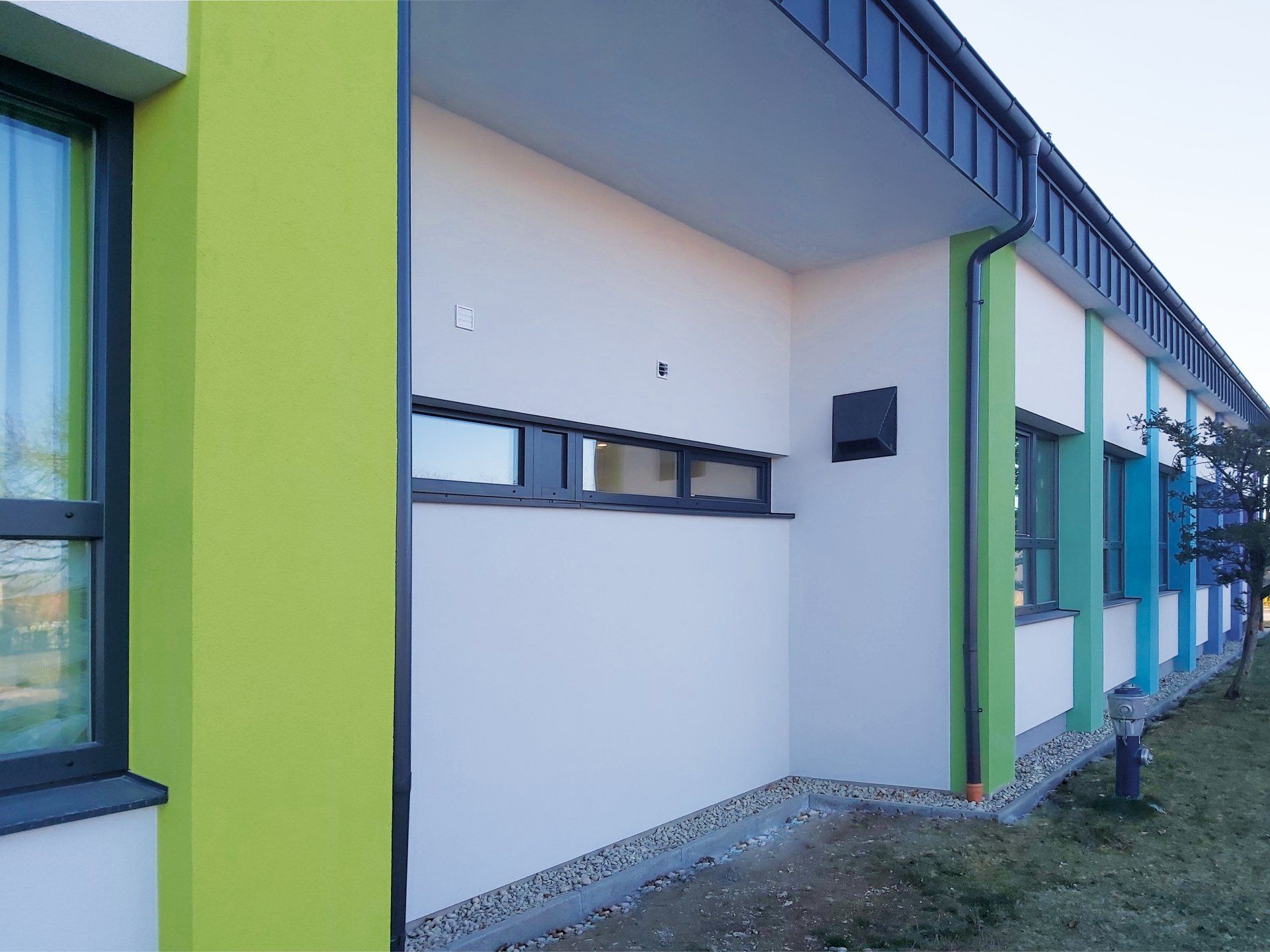 Außenansicht eines Gebäudes mit weißen und grünen Wänden, dunklen Fensterrahmen und einem schwarzen Dach.