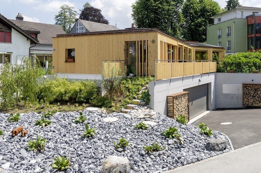 Holzhaus mit modernem Design, eingebauter Garage und einem mit Kies und Grünpflanzen gestalteten Garten.