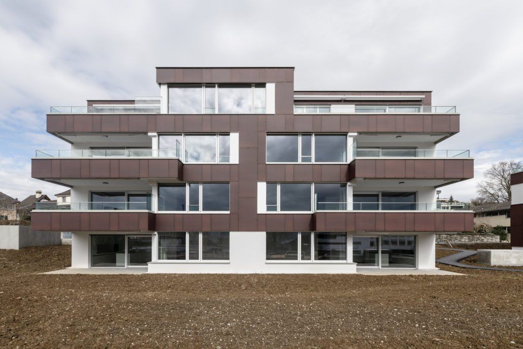 Modernes, braun-weißes, mehrstöckiges Wohnhaus mit großen Fenstern und Balkonen.