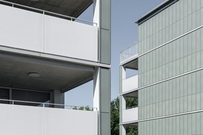 Zwei moderne Mehrfamilienhäuser mit Balkonen. Graue und grüne Fassade, blauer Himmel.