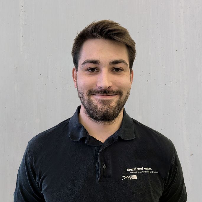 Mann in schwarzem Poloshirt lächelt in die Kamera, neutraler Hintergrund.