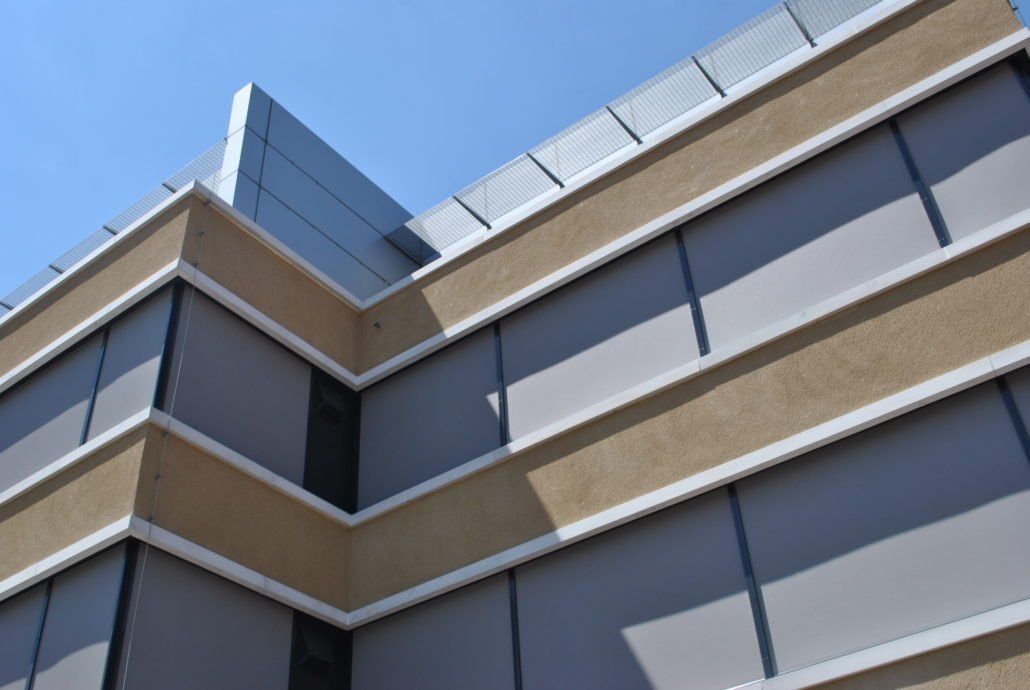 Modernes Gebäude mit beiger und grauer Fassade, großen Fenstern und blauem Himmel.