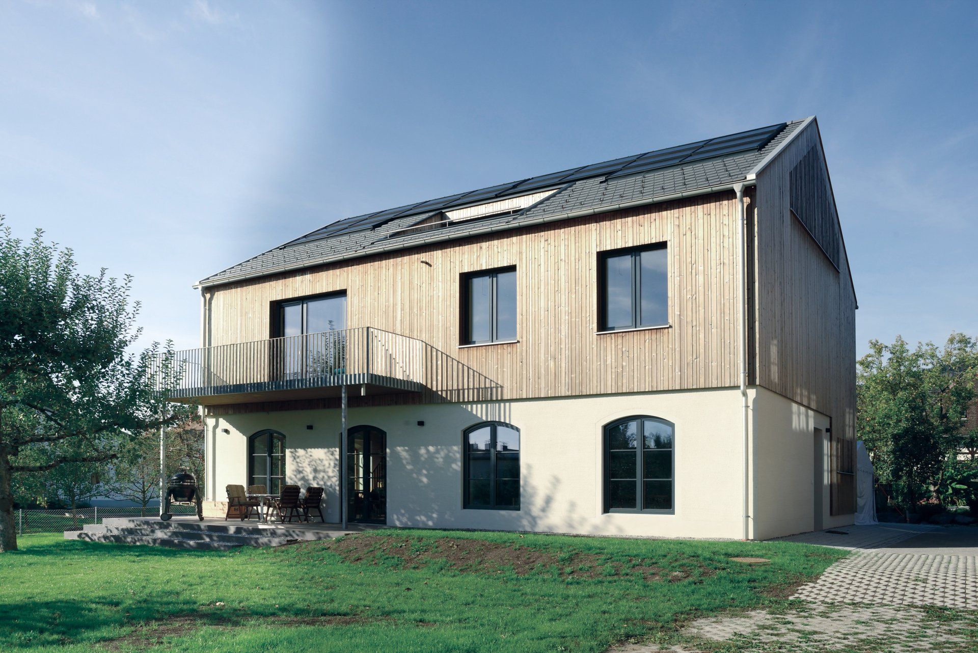 Modernes zweistöckiges Haus mit heller Holzverkleidung im oberen Bereich, weißem Stuck im unteren Bereich und einem kleinen Balkon.
