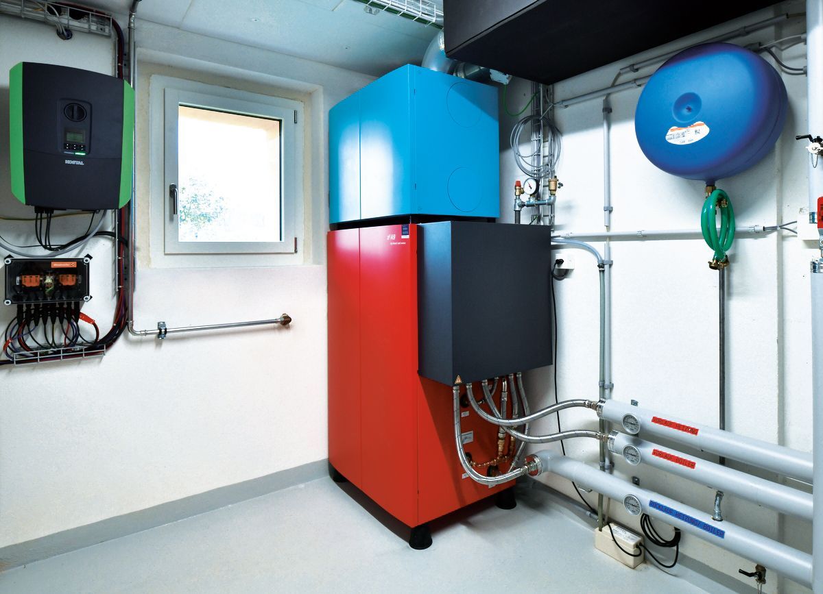 Ein Technikraum im Kellergeschoss mit Heizungs- und Elektroanlagen: rote, blaue und schwarze Einheiten mit Rohrleitungen.